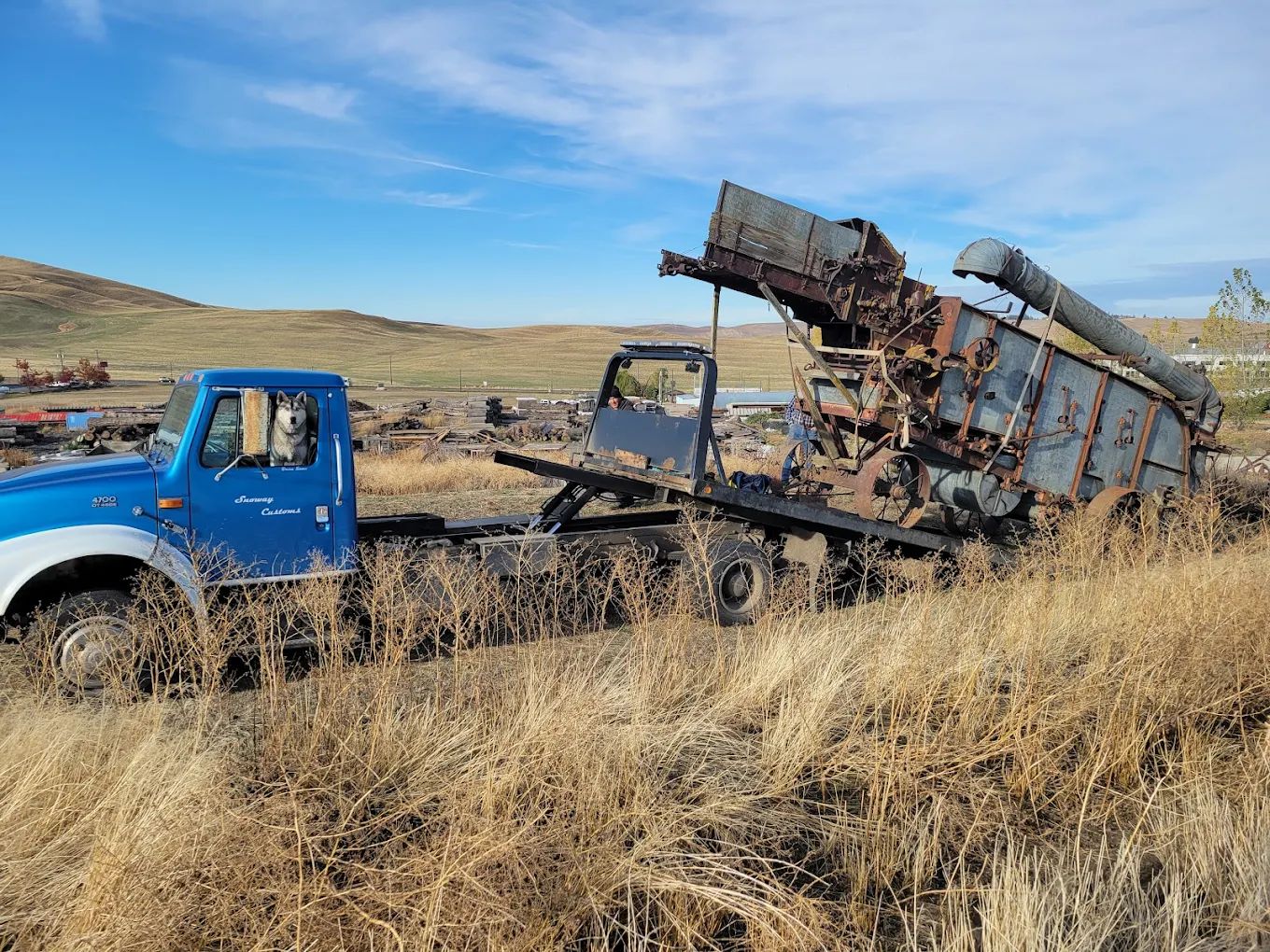Snoway flatbed loading antique farm machinery in a field